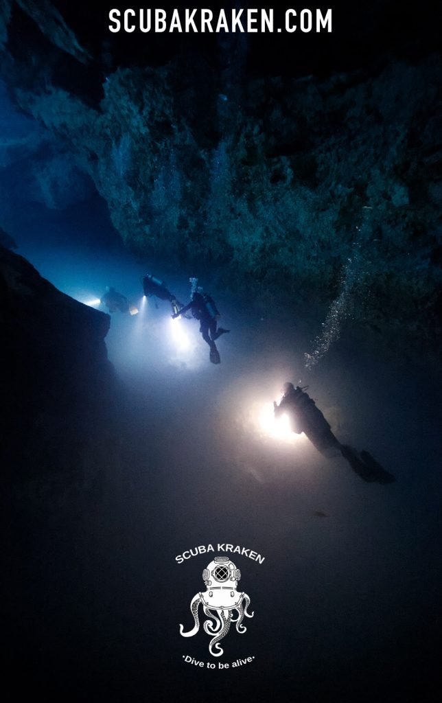Dos buzos con linternas en una caverna oscura de cenote entre haces de luz / Two divers with torches in a dark cenote cavern among light beams